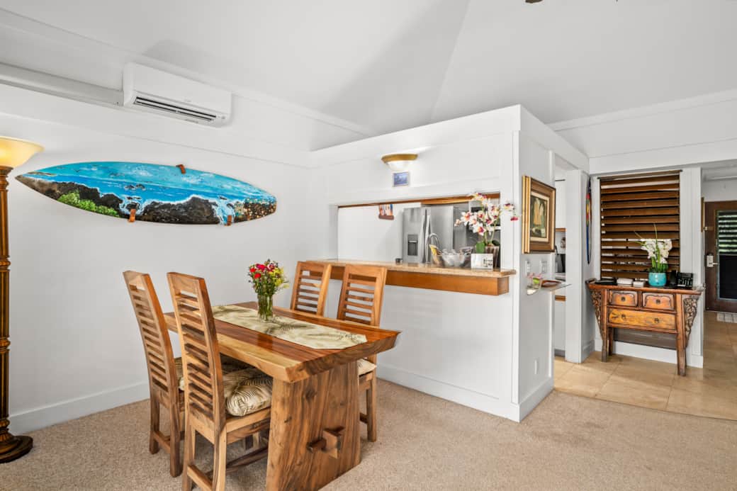 Cozy dining by the lanai, split A/C above, surfboard art—coffee with lush garden views just outside.