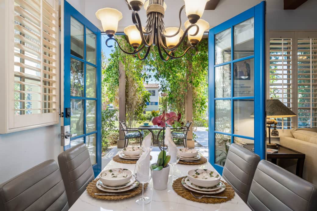 Dine in style with this elegant indoor-outdoor setup—blue French doors open to a lush patio garden