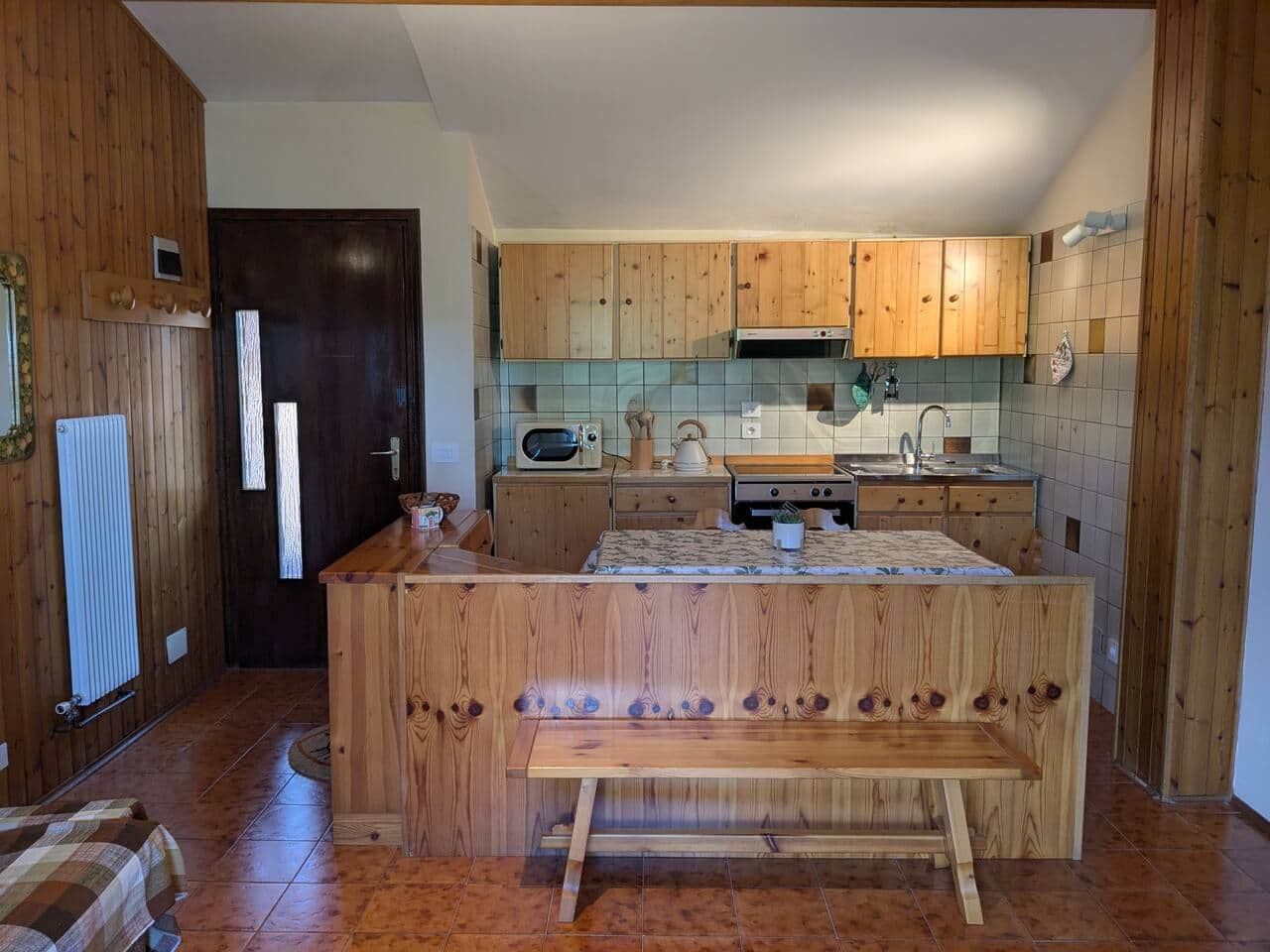 Cucina in legno con tavolo, panca, forno, piano cottura, bollitore e microonde