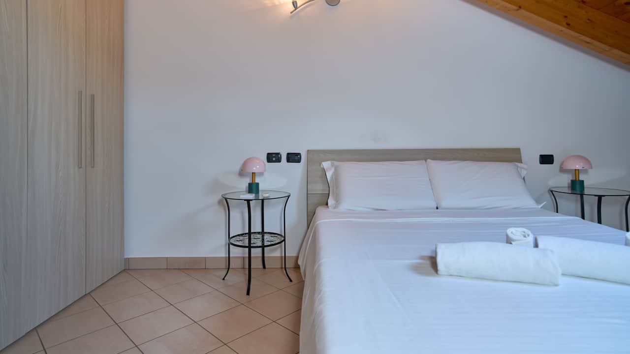 Dormitorio con cama blanca y pequeños estantes a los lados, en Monza