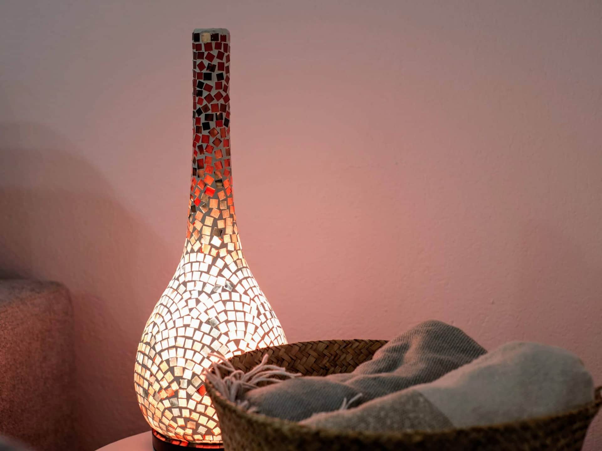 Lámpara de mosaico encendida que aporta luz cálida junto a cesta de mimbre con textiles en un rincón acogedor