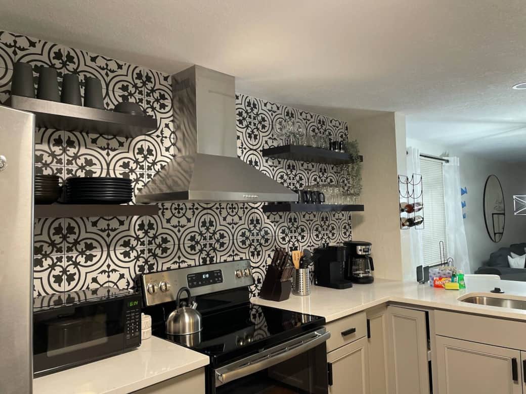 Stylish kitchen with Moroccan tile, floating shelves, and a modern stainless vent hood.