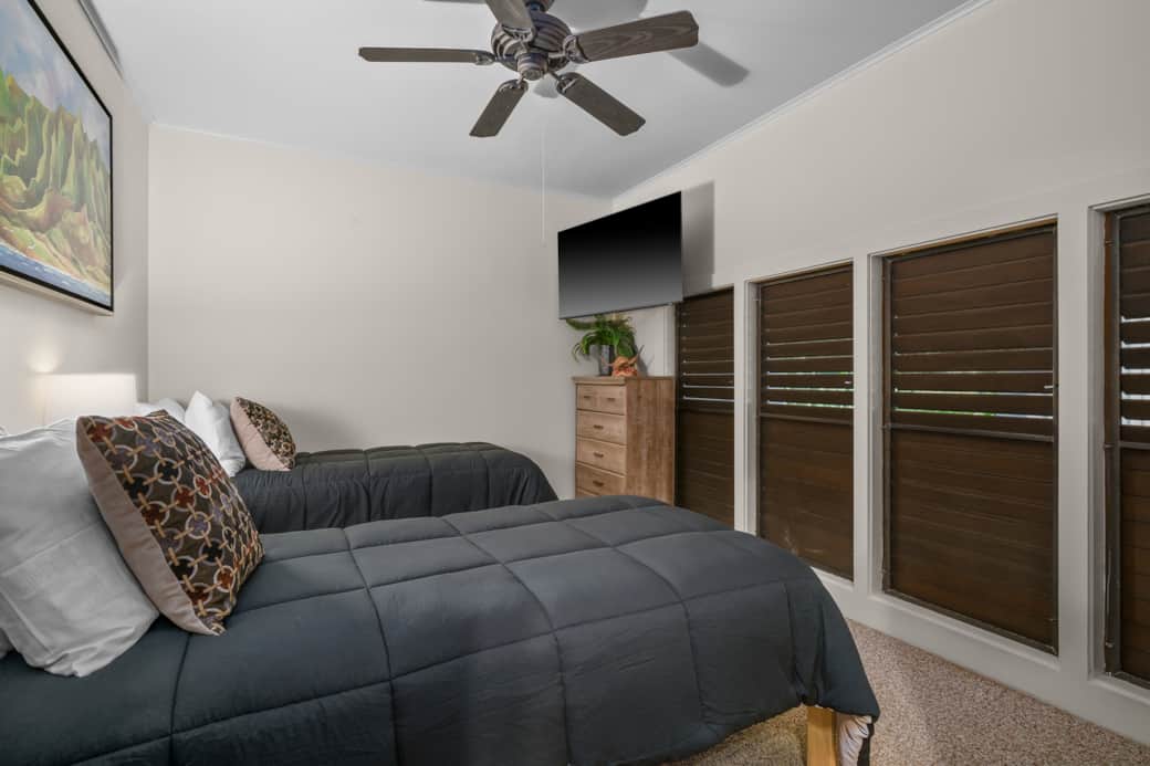 Comfortable twin setup with TV, AC, and plantation shutters for restful nights
