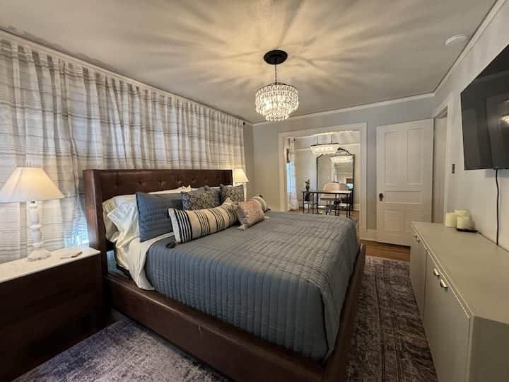 Spacious primary suite featuring a plush king bed, elegant chandelier.