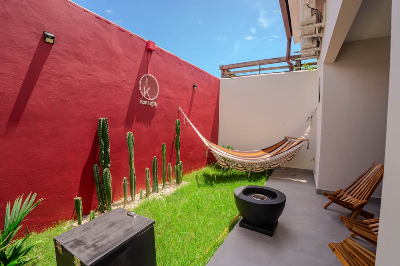 Sway in the hammock beside the bold red wall of our off-grid cabin garden in Pedasí.