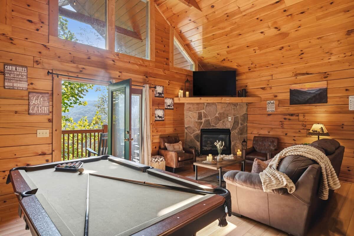 A cozy and inviting space featuring a nice view, a stone fireplace, warm wood accents, and comfortable leather seating. 