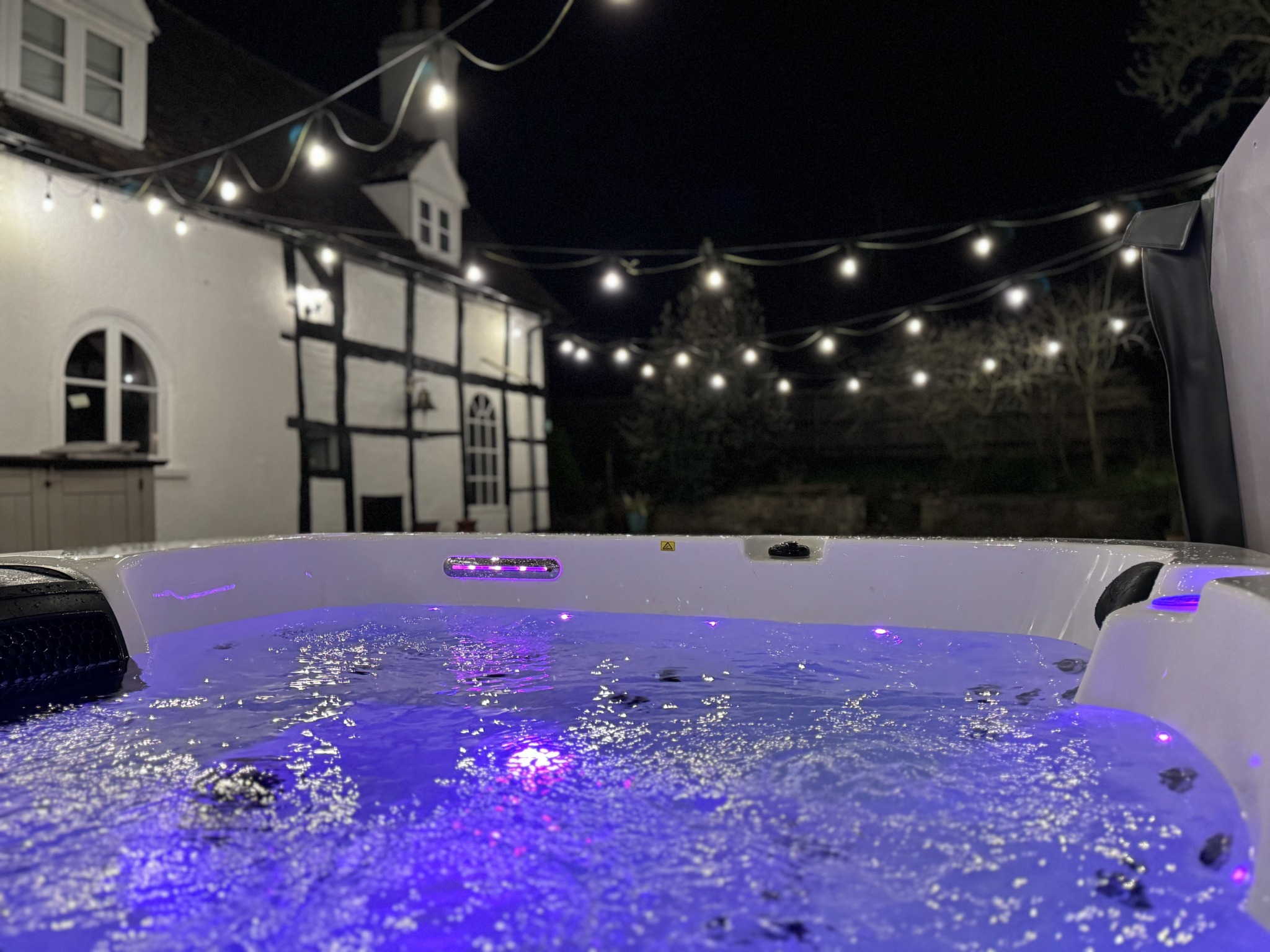 Six-person hot tub beneath evening lights at Evington House