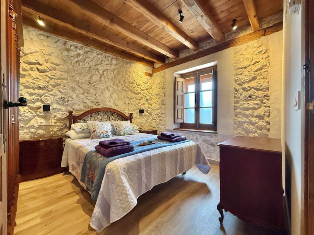 Dormitorio con cama de matrimonio, paredes de piedra y techo de madera que aportan calidez. Un espacio luminoso y confortable, ideal para relajarse tras un día de descanso o actividades en la zona. Dormitorio con cama de matrimonio, paredes de piedra y techo de madera que aportan calidez. Un espacio luminoso y confortable, ideal para relajarse tras un día de descanso o actividades en la zona.