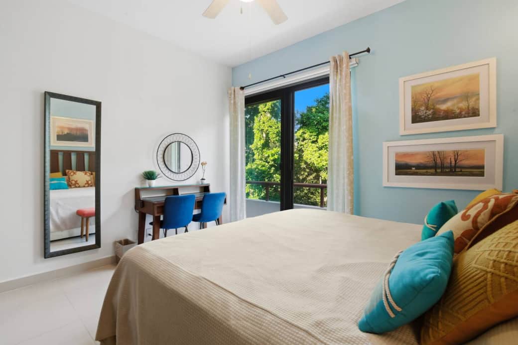 Bedroom 1 features a queen-size bed and direct access to your private balcony. Enjoy natural light, AC, ceiling fan, room-darkening shades, and a dedicated workspace with desk and two chairs for remote work.