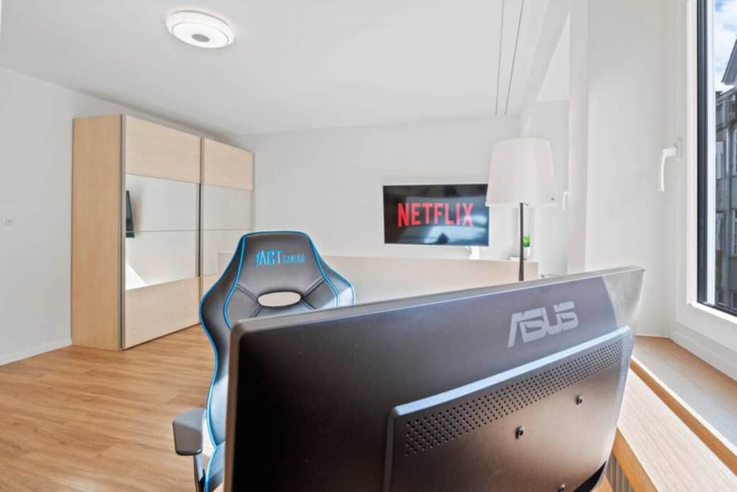 Bright workspace with gaming chair, external monitor and TV with Netflix in the background.