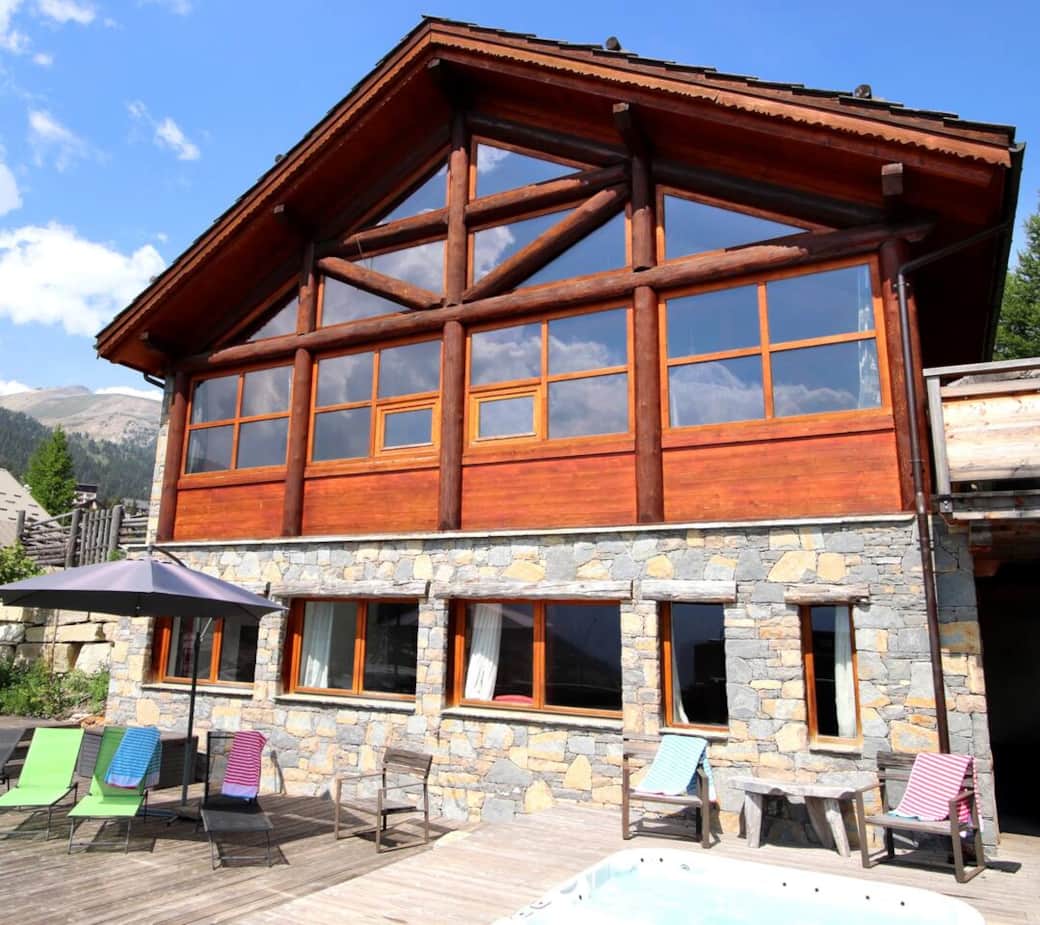 La façade principale du chalet et sa solarium accueillant le spa de nage, la table de ping pong, et bien sur des chaises longues pour travailler le bronzage d'été