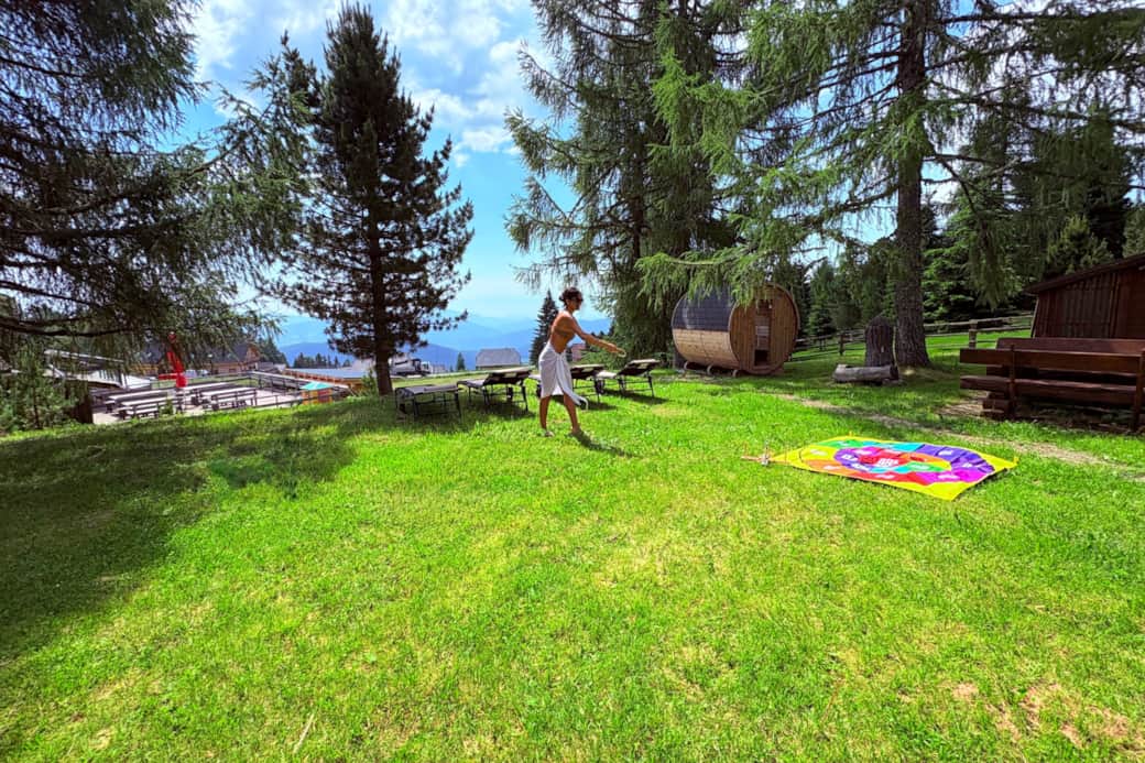 Sommerwiese mit Picknickdecke und Fasssauna vor Bergkulisse