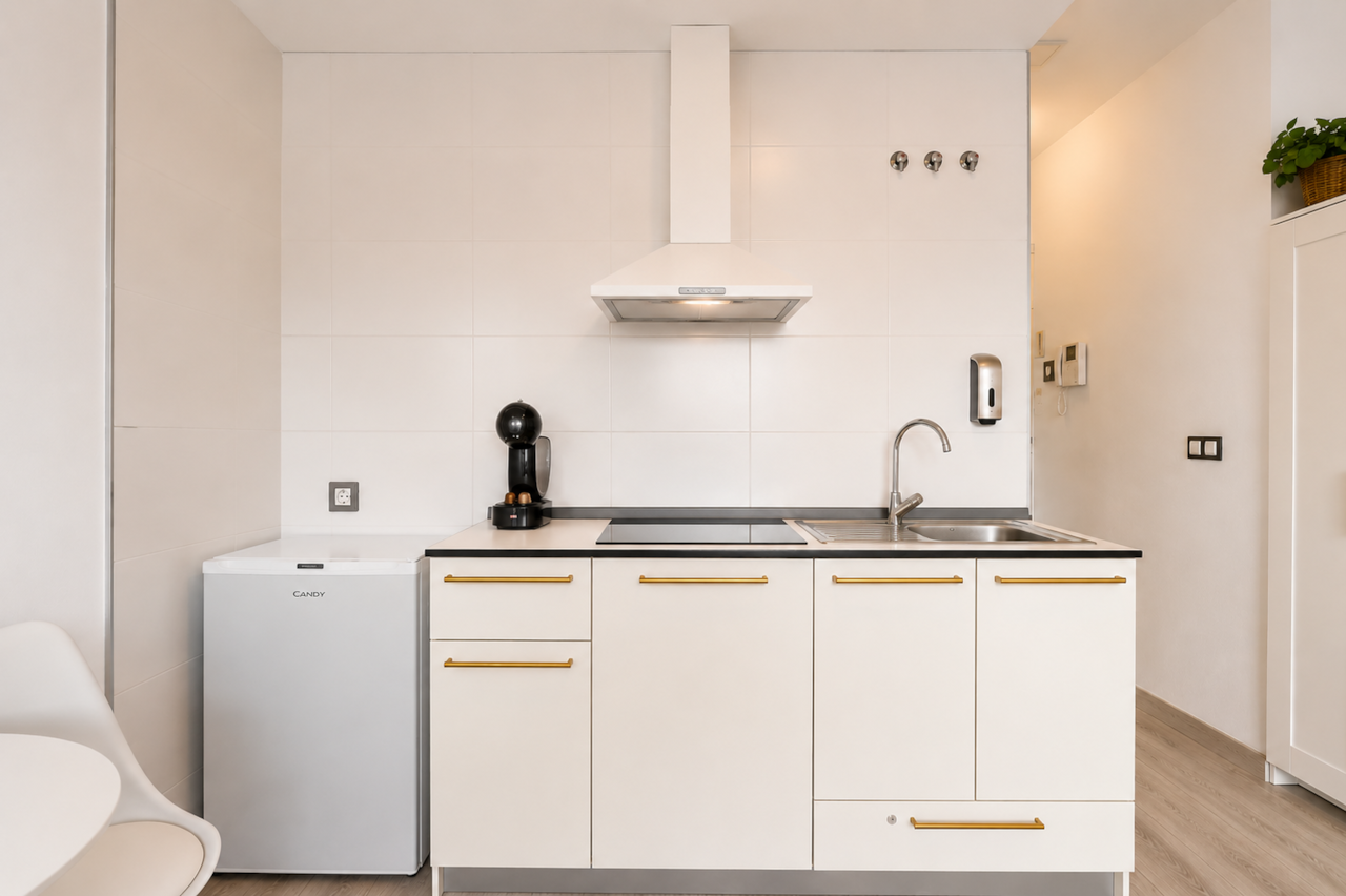 Compact kitchen with stovetop, fridge, extractor hood, and coffee machine.