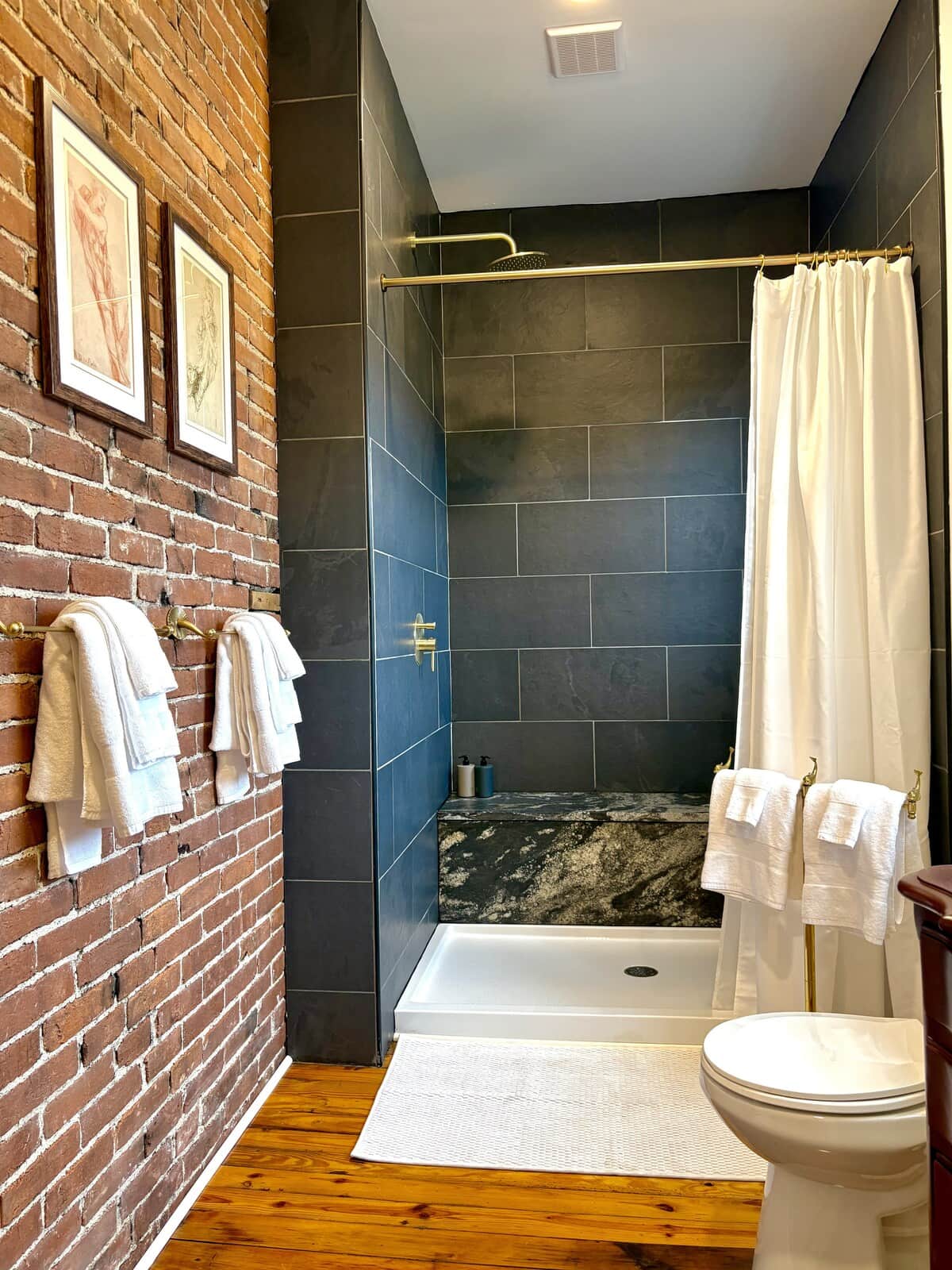 Slate tile, exposed brick, and a brass rainfall shower with a marble bench built for lingering