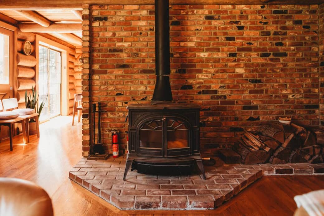 A two-story tall wood fire stove sits in the main living room with firewood and fire starters provided. A two-story tall wood fire stove sits in the main living room with firewood and fire starters provided.
