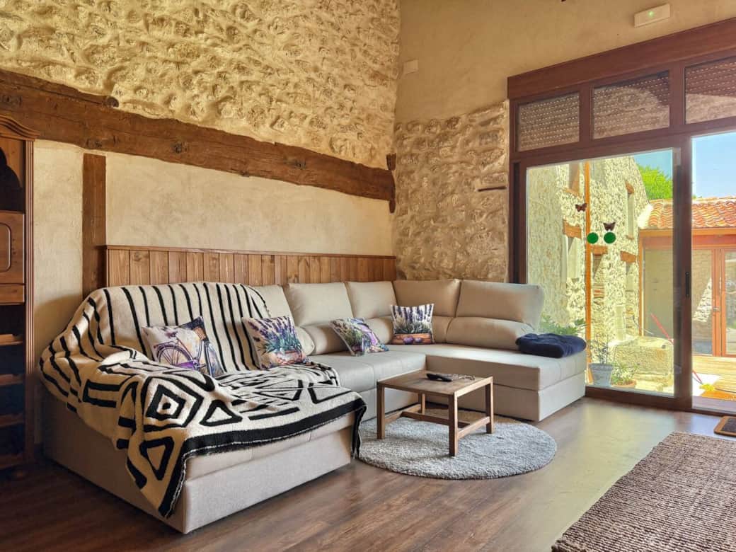 Amplio salón con sofá chaise longue, decoración rústica y grandes ventanales que llenan de luz el espacio, creando un ambiente cálido y acogedor para compartir en grupo.