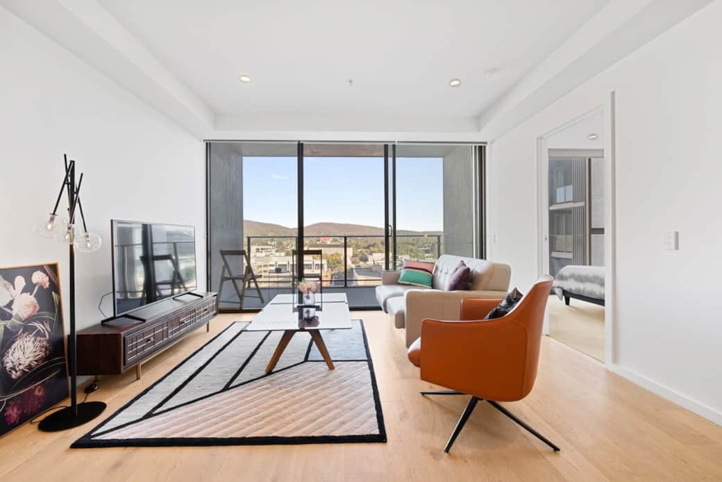 This vibrant living room is a perfect blend of comfort and style. The plush beige sofa and striking orange armchair invite relaxation. The geometric rug adds a modern touch, while the large windows offer a breathtaking view of the city skyline. 