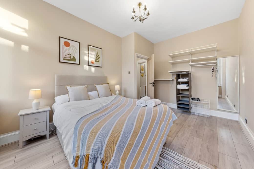 Spacious and beautifully presented bedroom with a new comfortable double bed, new quality mattress, soft linens, and elegant bedside lighting. Large sash windows fill the room with natural light, while the open-plan wardrobe enhances space and flow.