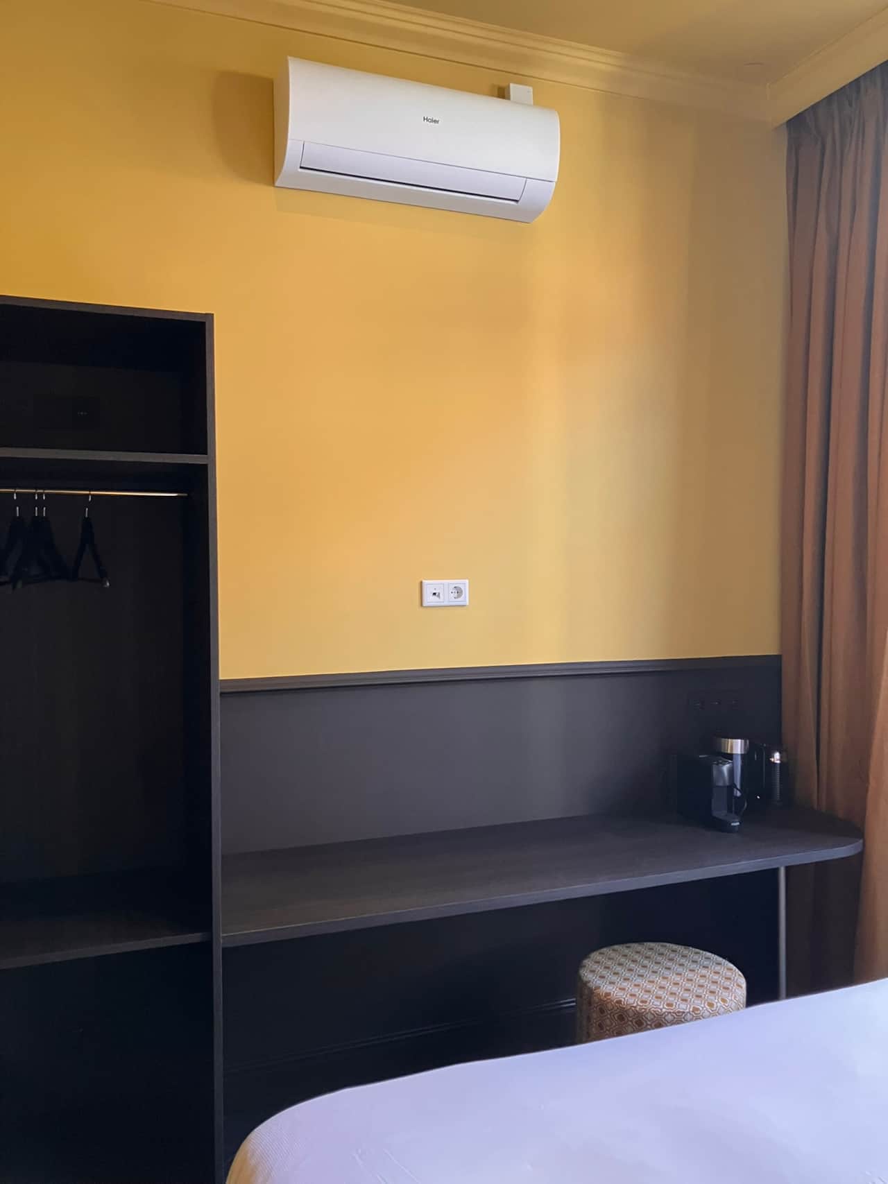 Aleida Suite desk and open wardrobe against a mustard-yellow wall, with tea and coffee station