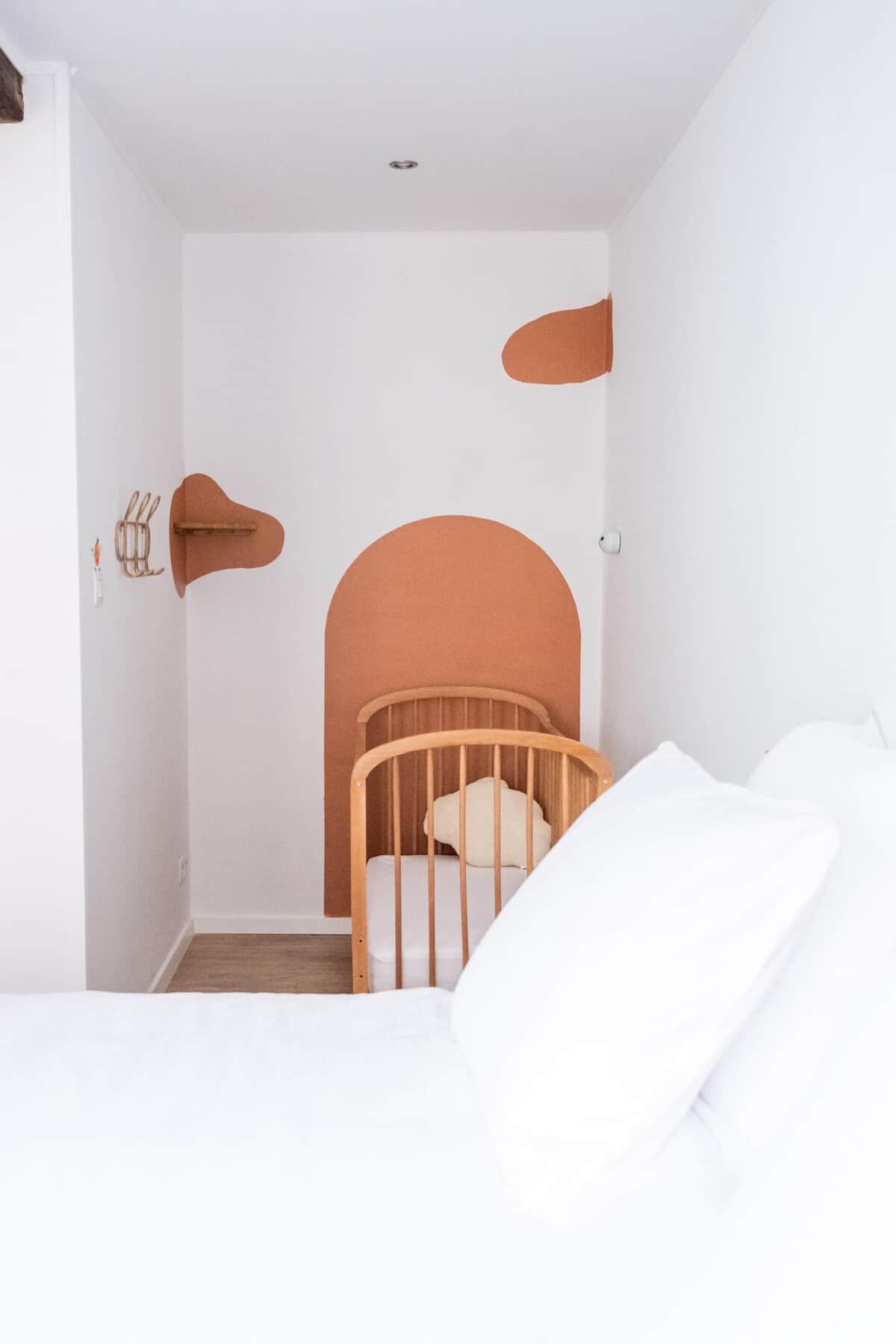 Lit bébé présent dans la chambre. Il y a également une veilleuse, une tablette pour le babyphone et des patères pour pendre les affaires de bébé. 