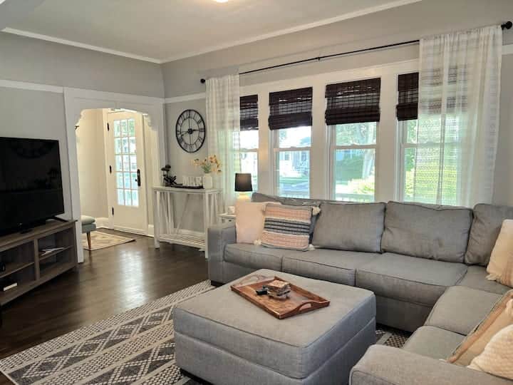 Bright and cozy living room featuring a spacious sectional sofa, soft lighting, and large windows.