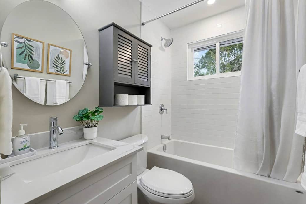 Fully renovated bathroom includes a single vanity, quartz countertop and chrome finishings. The bathtub/shower is tiled with a small window to allow natural light to fill the space.