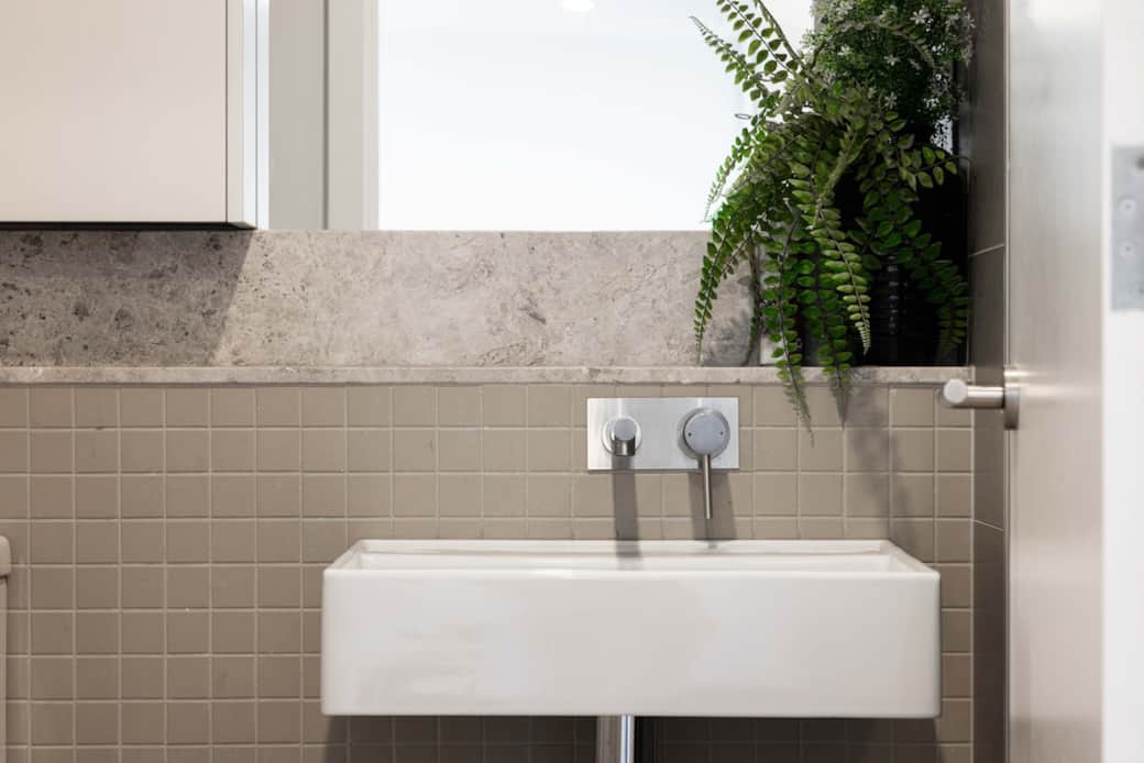 The bathroom features a sleek, wall-mounted sink and a stylish mirror cabinet. The neutral color palette and clean lines create a sense of spaciousness. A touch of greenery from the window adds a refreshing touch to the modern decoration.