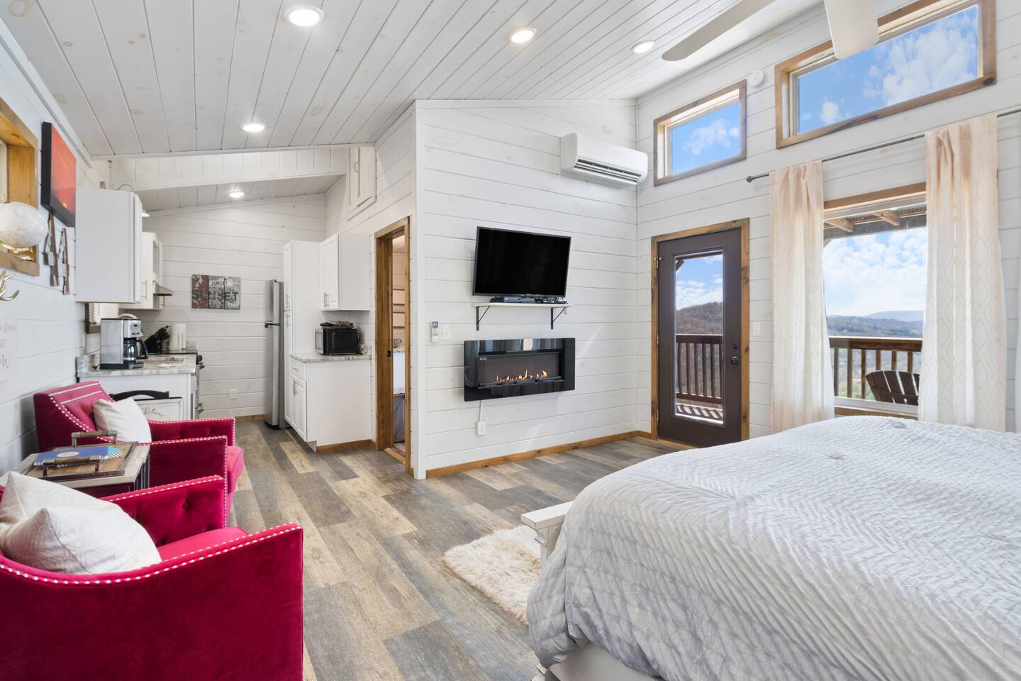 A wide-angle view of a cozy studio room with a kitchenette, fireplace, and mountain view.