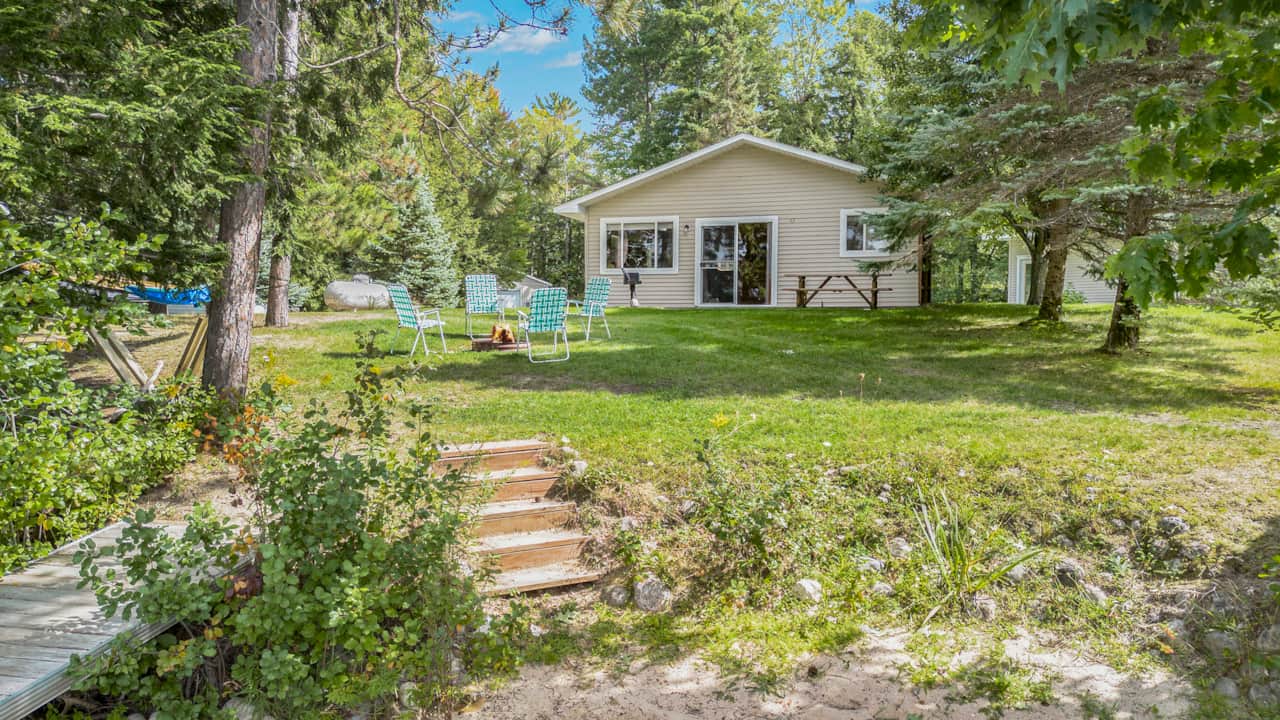 Lakefront lawn with firepit and picnic table, steps down to the beach for swimming and fishing