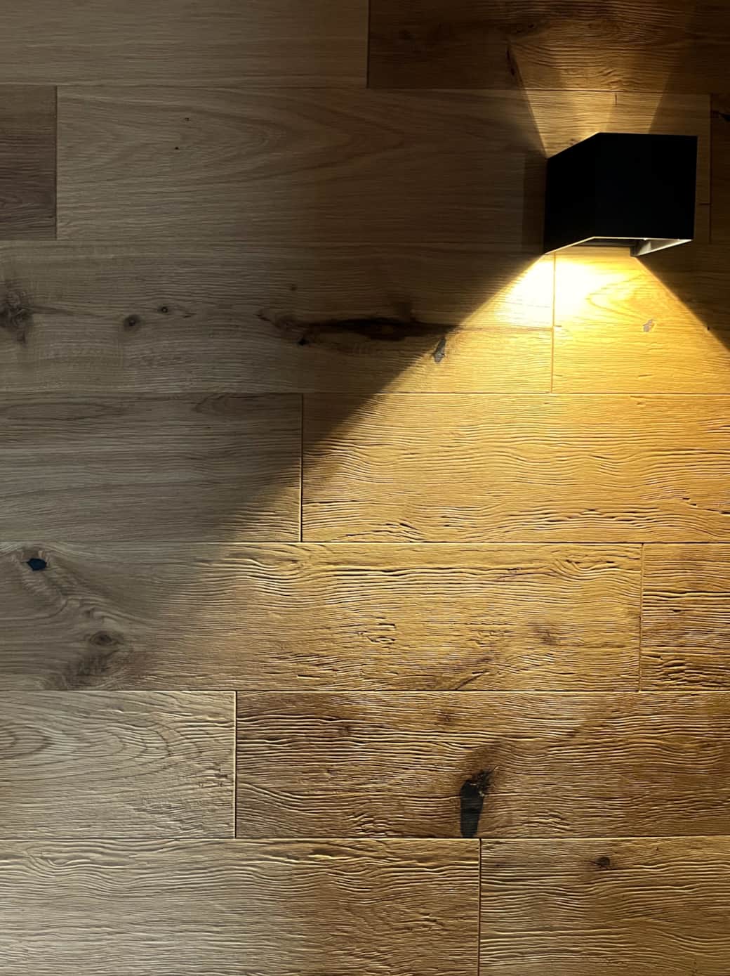 Holz, das Wärme ausstrahlt: Angestrahltes Eichenholz als Rückwand hinter dem Bett.