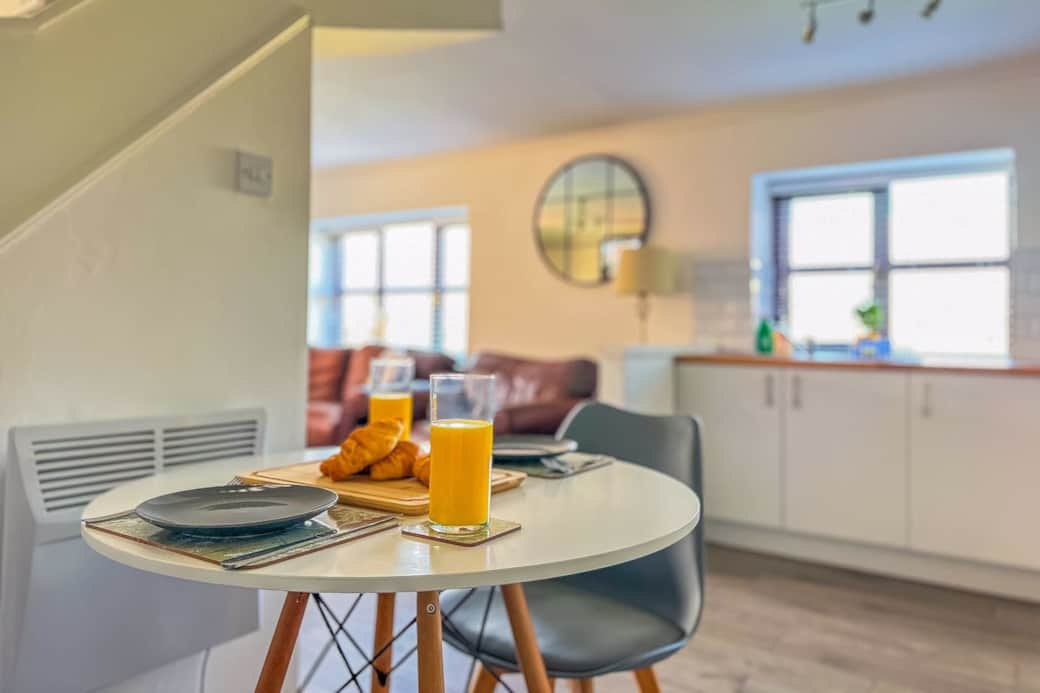 Dining table set for breakfast with fully equppied kitchen and living room in the background