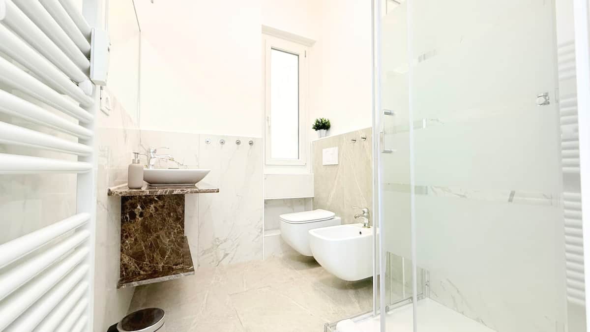 Bagno sofisticato con finiture in marmo e box doccia in vetro: un angolo di benessere!