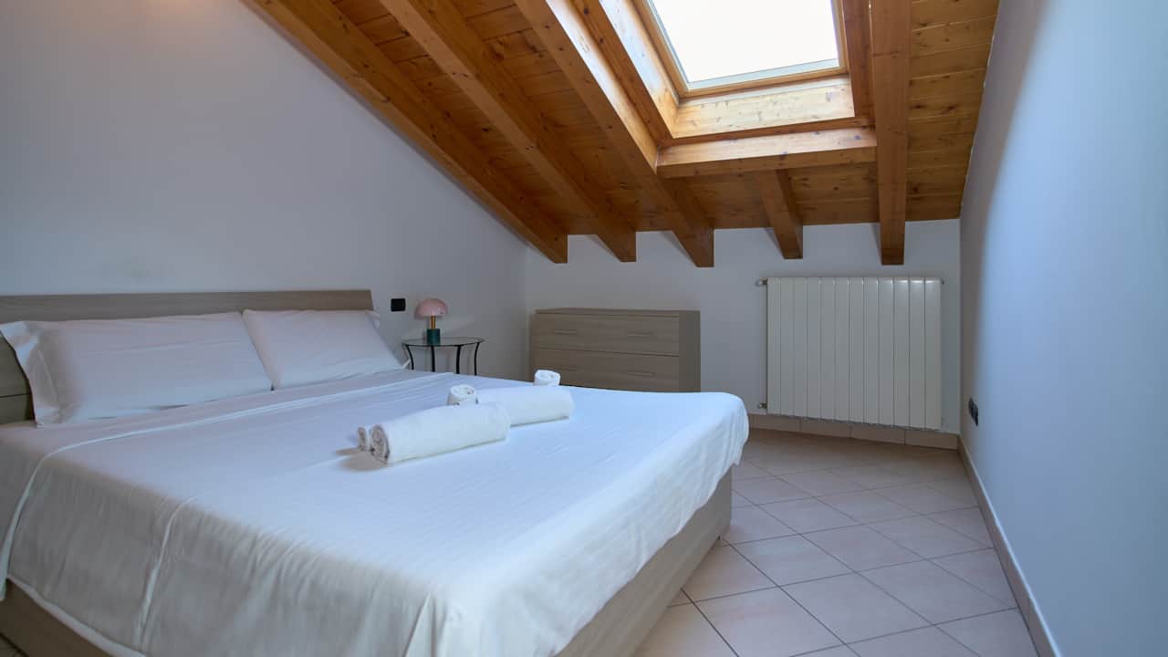 Bett unter dem Holzdach mit Bullauge und Heizkörper