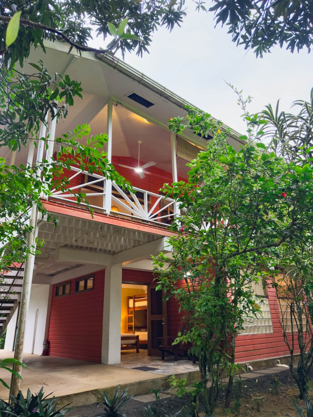 Corner exterior view of Conchy Tonk showcasing the elevated second floor, covered terrace, and garden-level entrance framed by tropical greenery.
