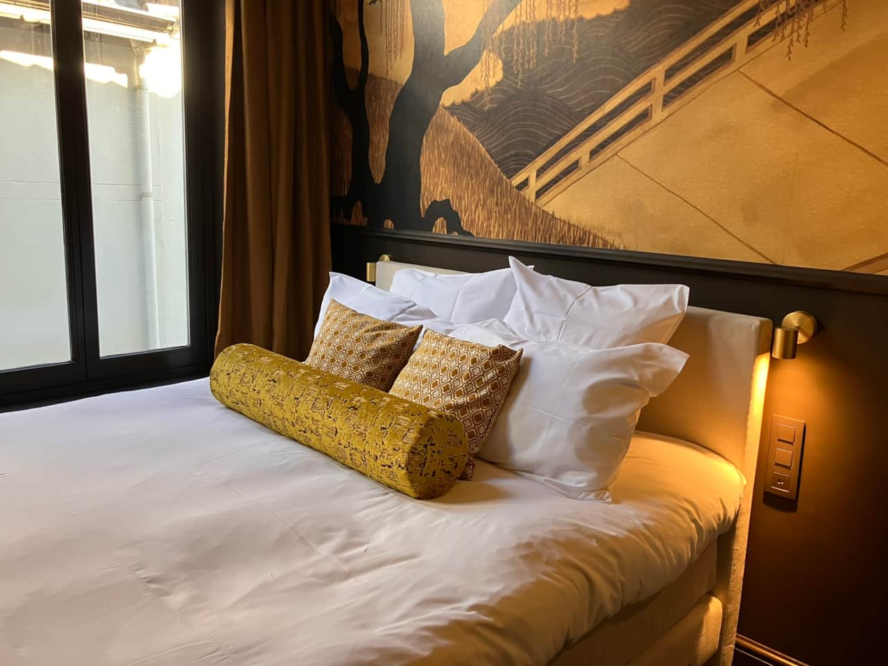 Aleida Suite bed with mustard velvet cushions below a wallpaper mural, Gilded Ox Suites Deventer