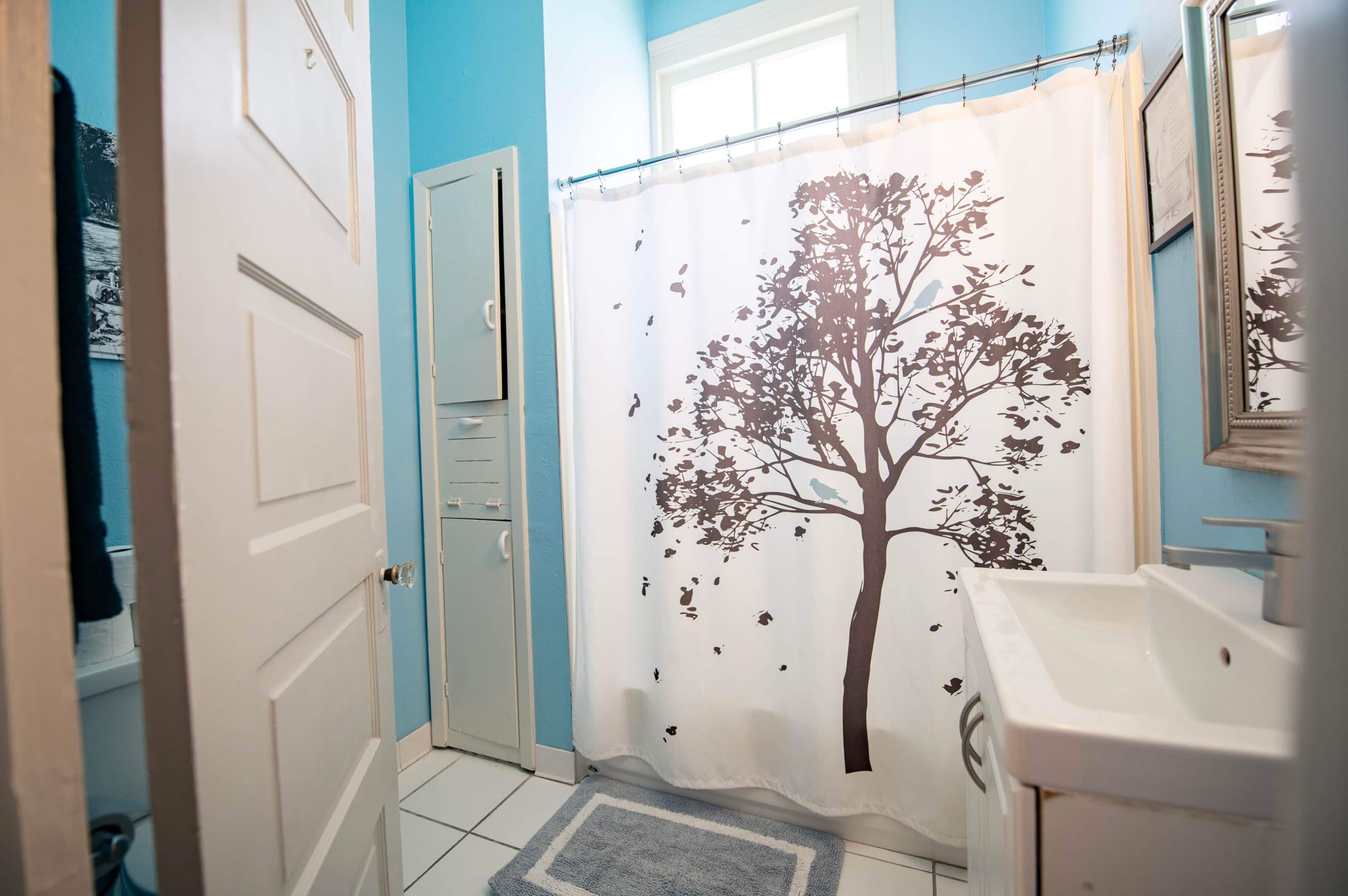 A bathroom with blue walls, a white sink, and a shower curtain with a tree design.