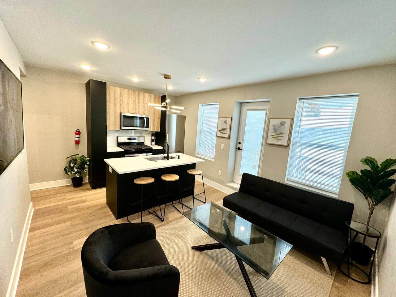 Modern kitchen featuring brand-new appliances, including a breakfast bar, dishwasher, microwave, and refrigerator. It seamlessly connects to the living room, which is furnished with a sofa bed, and a large flat-tv.
