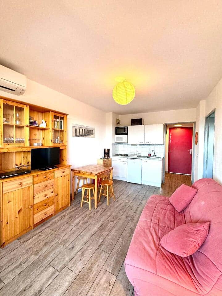 Séjour lumineux et chaleureux, avec mobilier en bois, canapé confortable, TV et coin repas. Kitchenette équipée (plaques, micro-ondes, frigo, cafetière). Atmosphère cosy, idéale pour profiter du port d’Argelès.