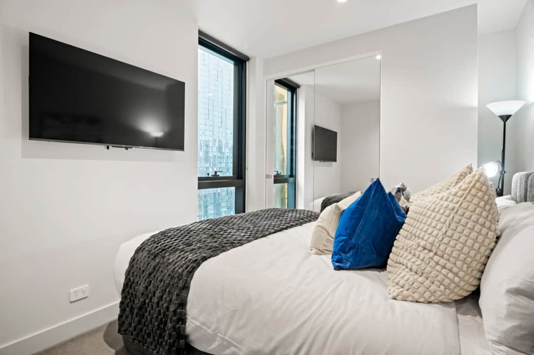 A modern and well-designed bedroom with a comfortable bed, premium linens, and a Smart TV for entertainment. Complete with a mirrored wardrobe and natural light, offering both comfort and functionality.