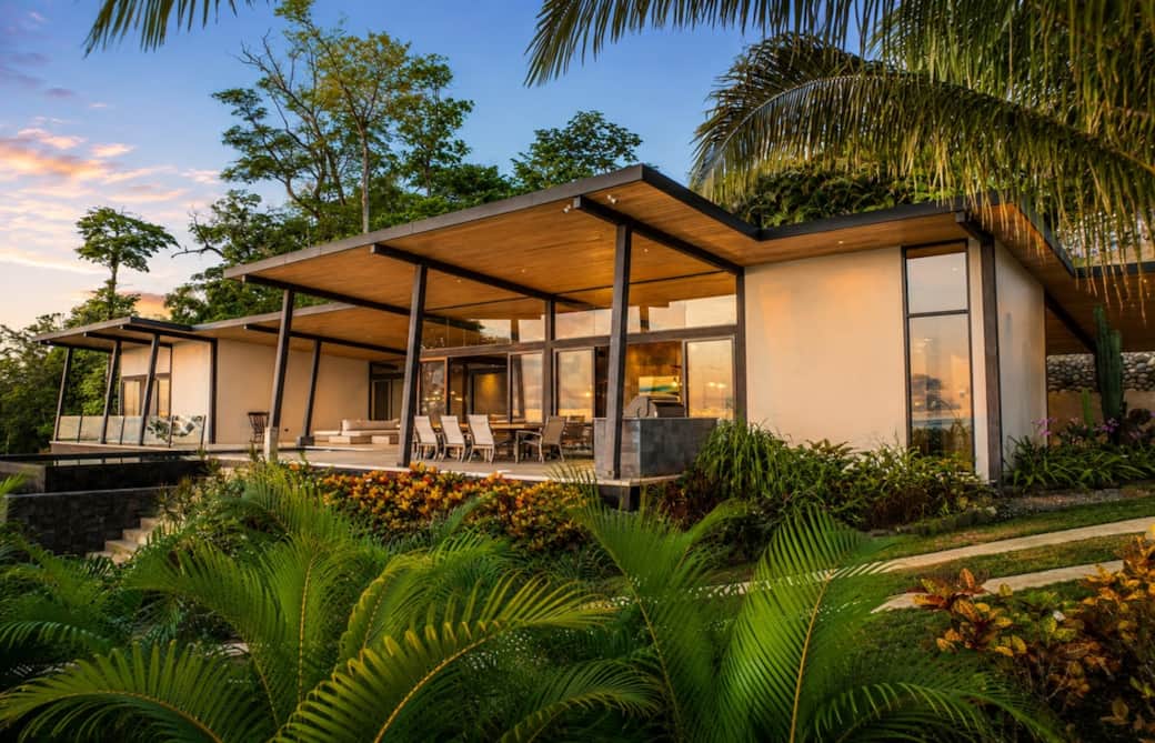 A striking architectural masterpiece surrounded by lush tropical gardens, where contemporary design, warm evening light, and seamless indoor-outdoor living create an unforgettable luxury retreat in Costa Rica.
