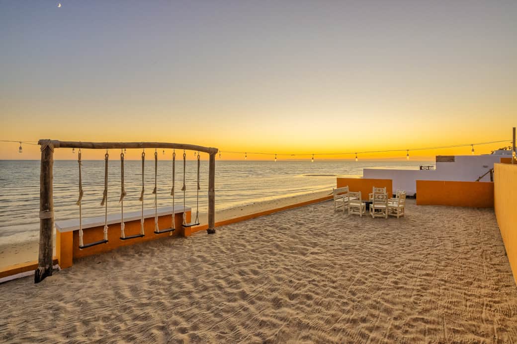 Beachfront bar with swings overlooking the Sea of Cortez during sunset.