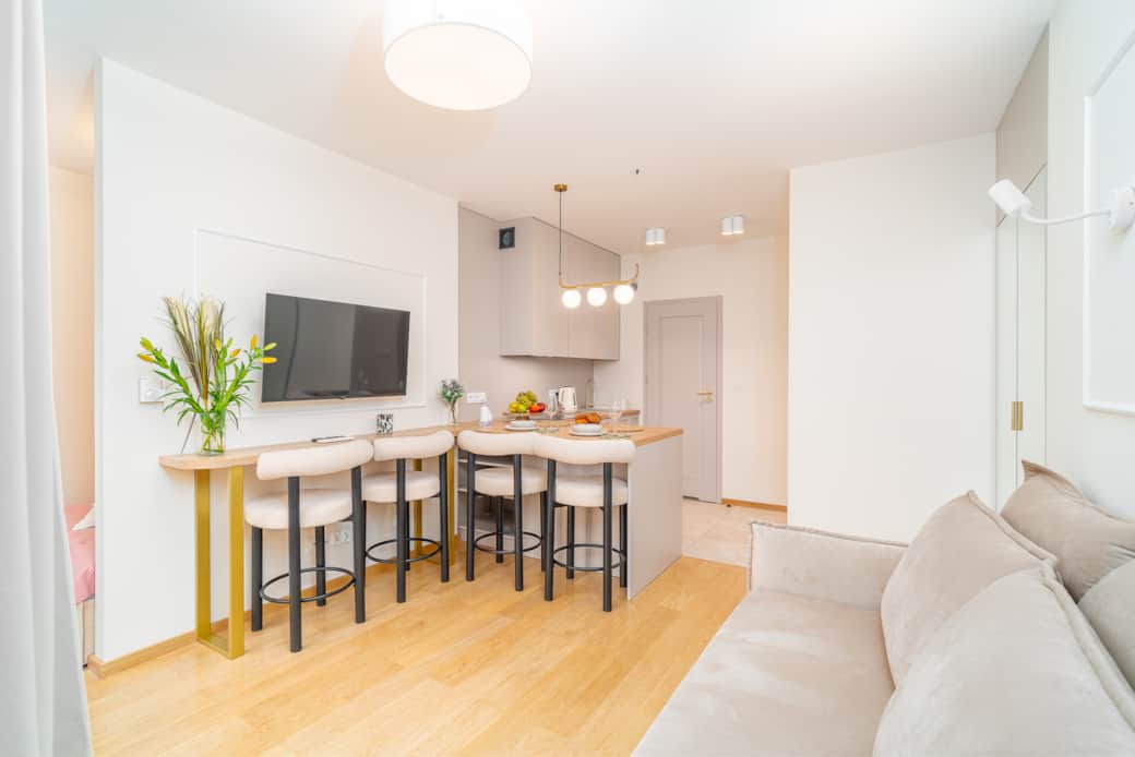 Nowoczesny salon z aneksem kuchennym i stołem barowym, utrzymany w jasnych, ciepłych tonach.