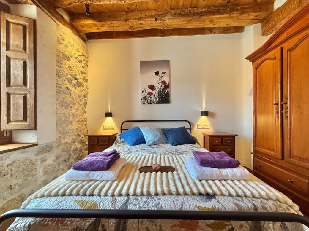 Dormitorio acogedor con cama de matrimonio, muebles de madera y paredes de piedra que realzan el encanto rústico. Un espacio cálido y tranquilo para descansar.