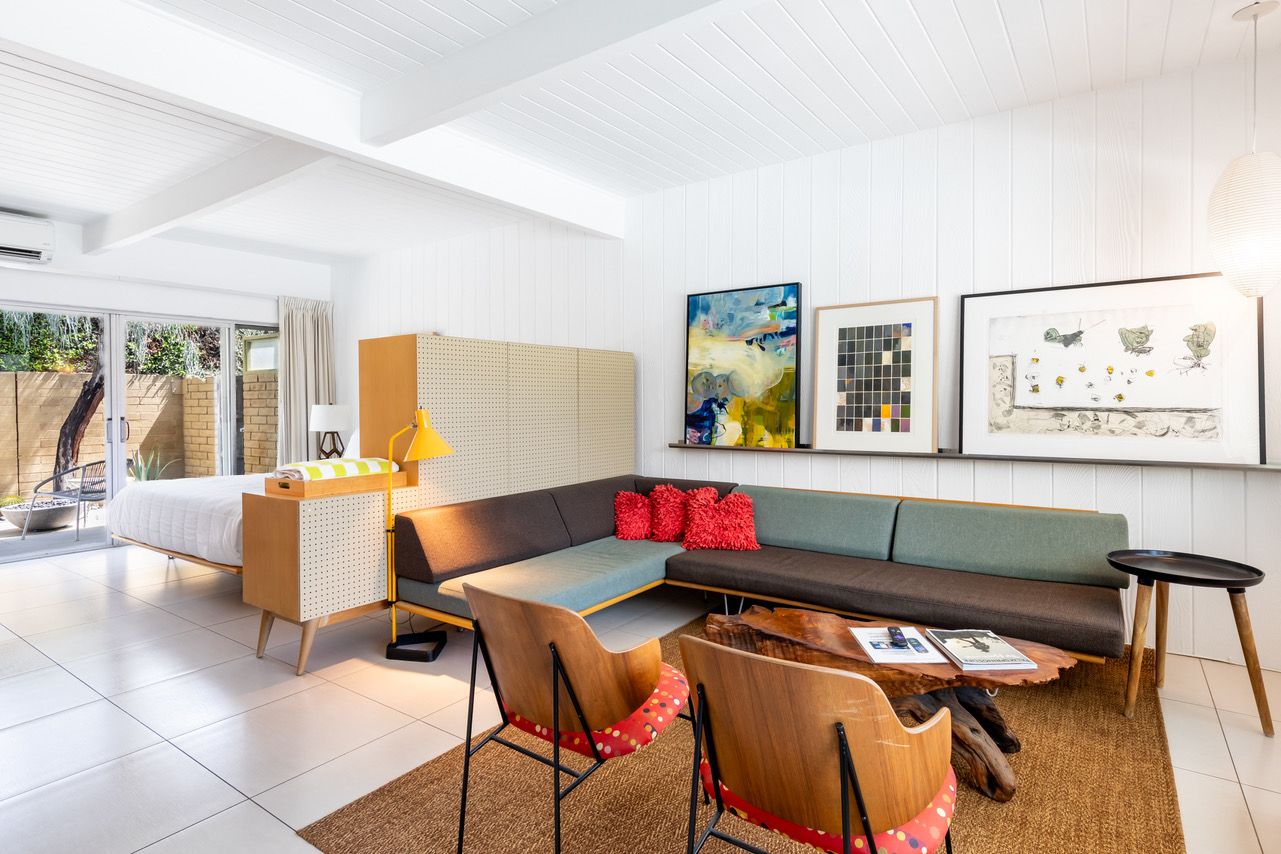 A wide view of a studio room with a sofa, coffee table, chairs, bed, and artwork on the walls.