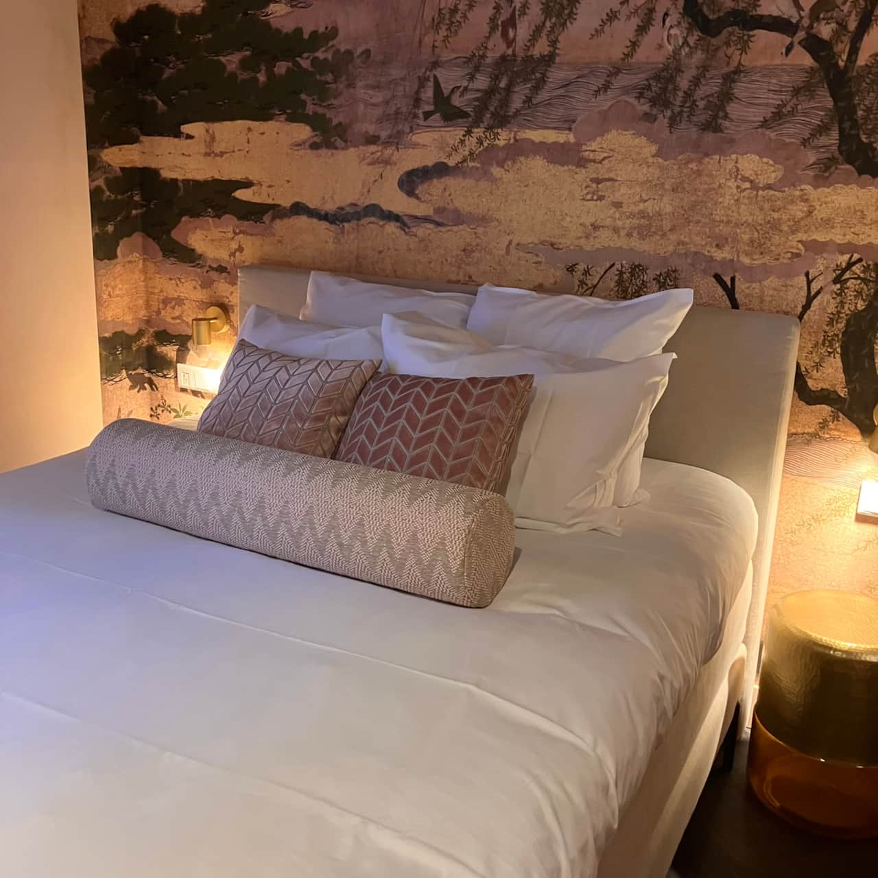 Robinah Suite bed with a rose herringbone bolster, below a Japanese wallpaper mural