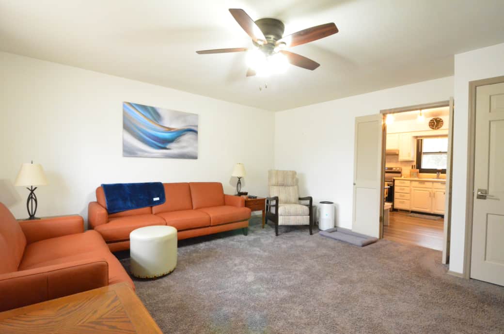 Living room with seating for 6, a recliner and a large Roku TV. Hallway to the bedroom on the right.