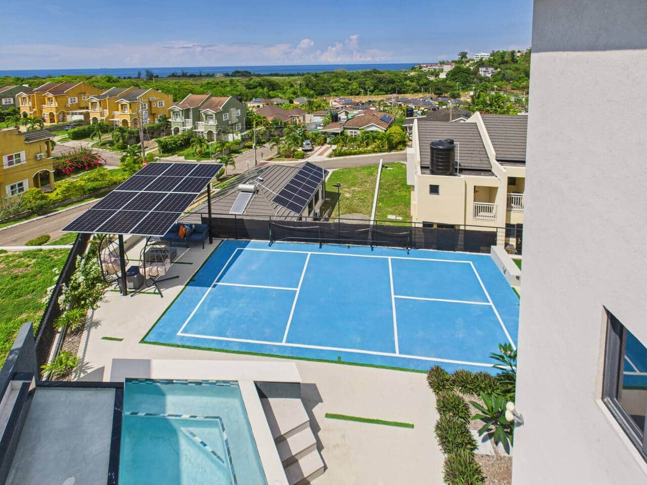 Terrace view of the villa’s private recreation area featuring a mini pickleball court, sparkling pool, and solar-powered lounge spaces, all set against views of the Caribbean Sea.
