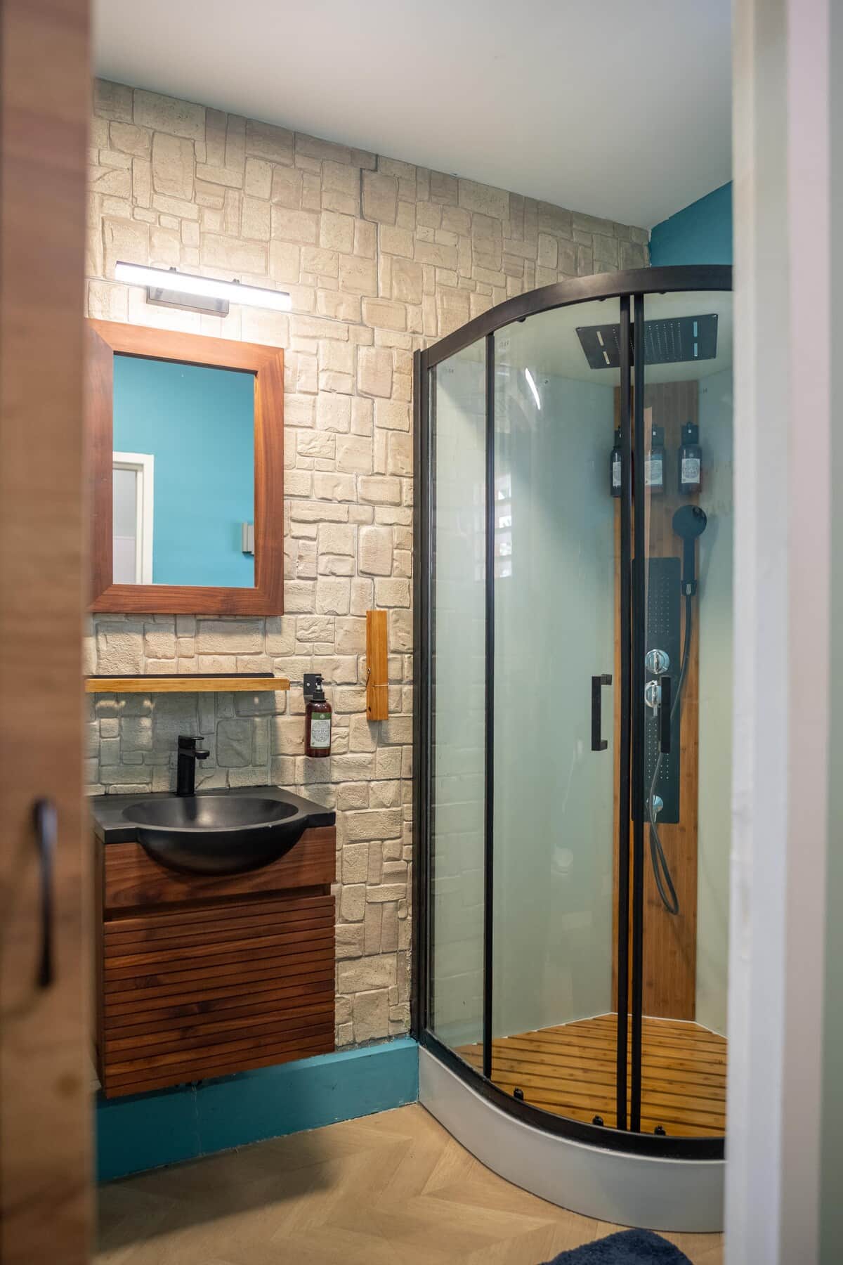 Salle de bain avec douche, murs en pierre et miroir bleu