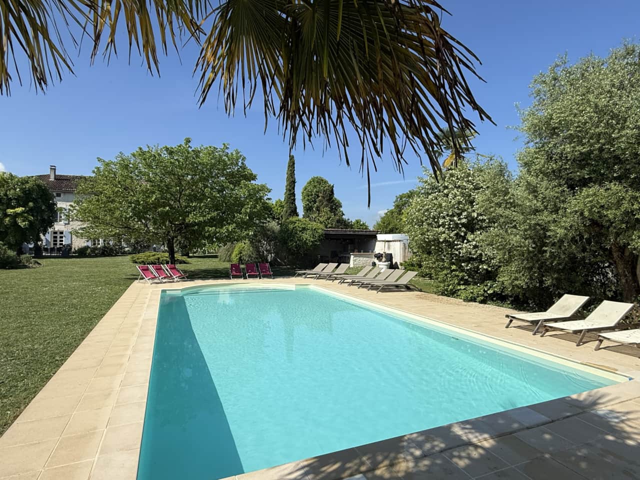Blick auf den Pool mit Liegestühlen und Poolhaus