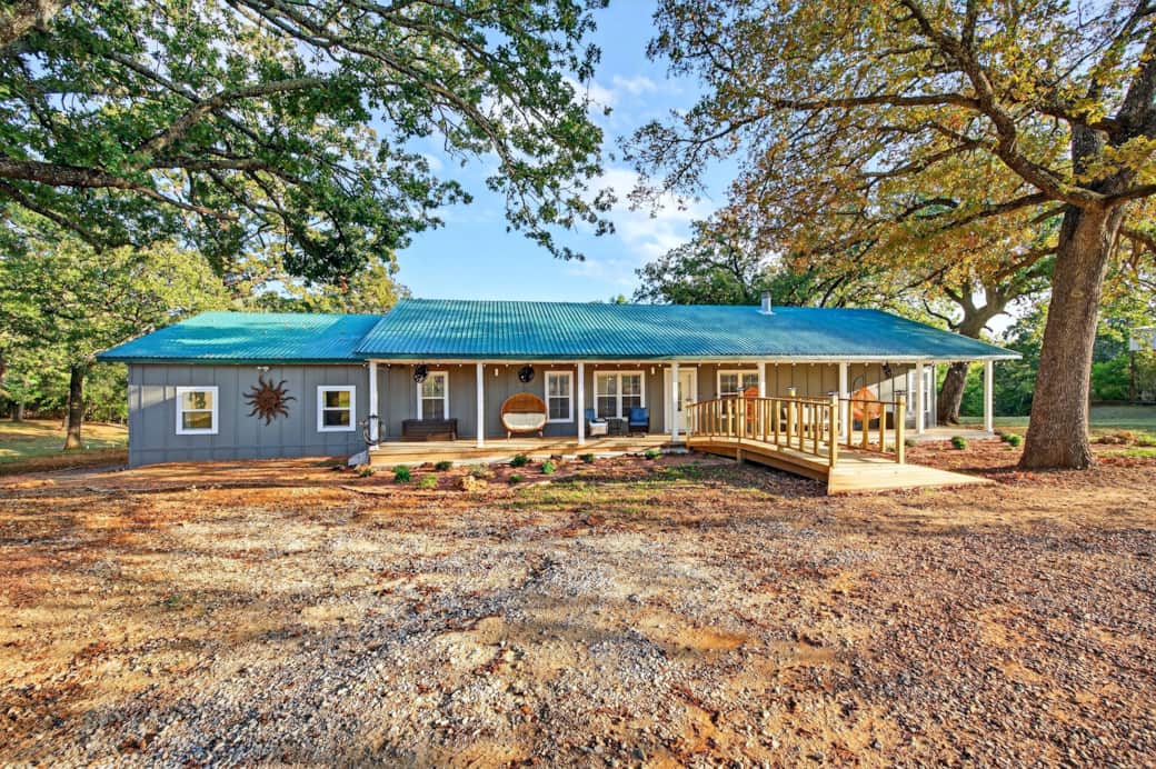 Front exterior with wraparound porch, shaded by mature trees